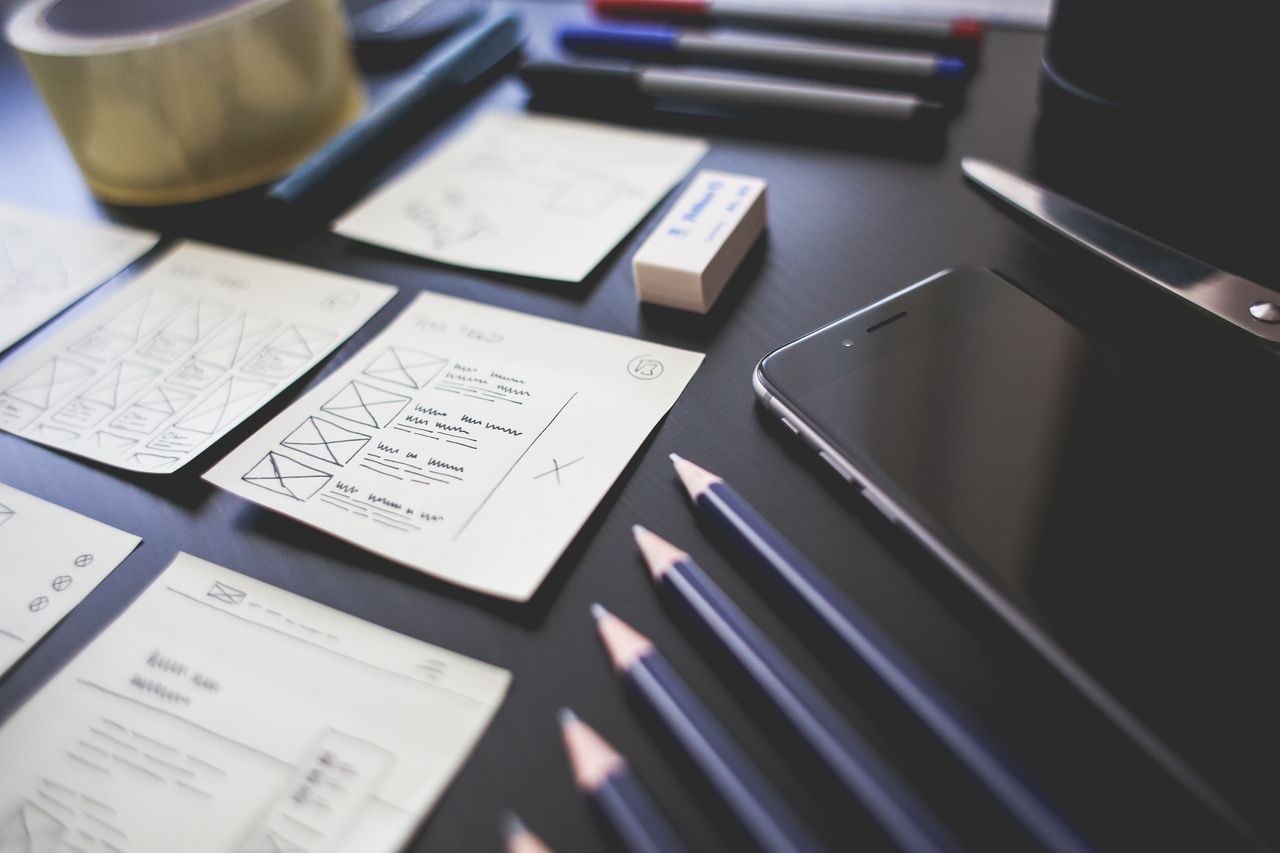 services-04 A creative workspace featuring UI design plans, pencils, a smartphone, and other office tools.